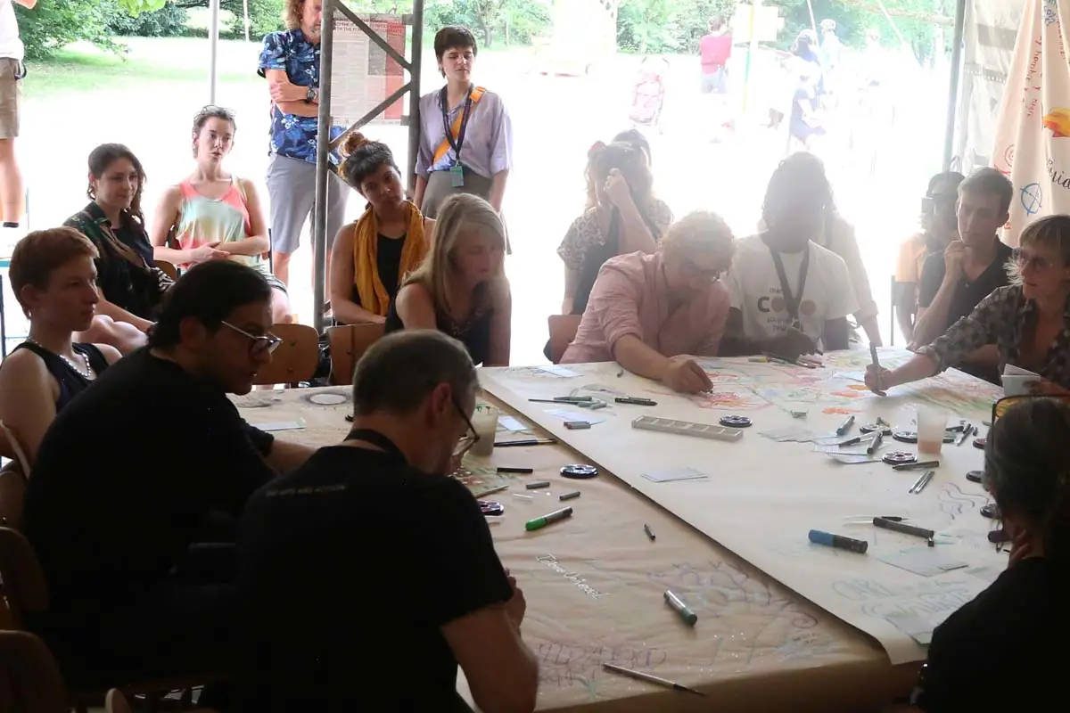 ten people drawing round a large table with audience at Documenta festival, Germany